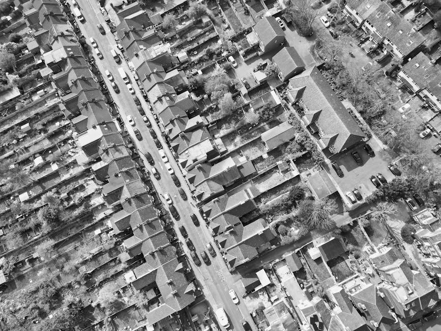 An aerial view of a residential neighborhood on Crowndale Road in Kentish Town, showing a row of terraced houses with sloped tiled roofs, narrow streets lined with parked cars, and trees interspersed throughout the area. The image captures the layout of the neighborhood with houses closely packed together, some with small front gardens or yards, and the street illuminated by natural daylight. As part of domestic cleaning and surface cleaning services offered by Cleaners Kentish Town, such detailed maintenance ensures the area's cleanliness and hygiene, supporting a safe and tidy environment for residents.